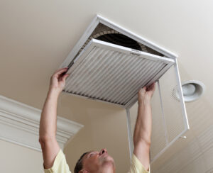 A technician reaching up to open filter holder for air conditioning filter in ceiling