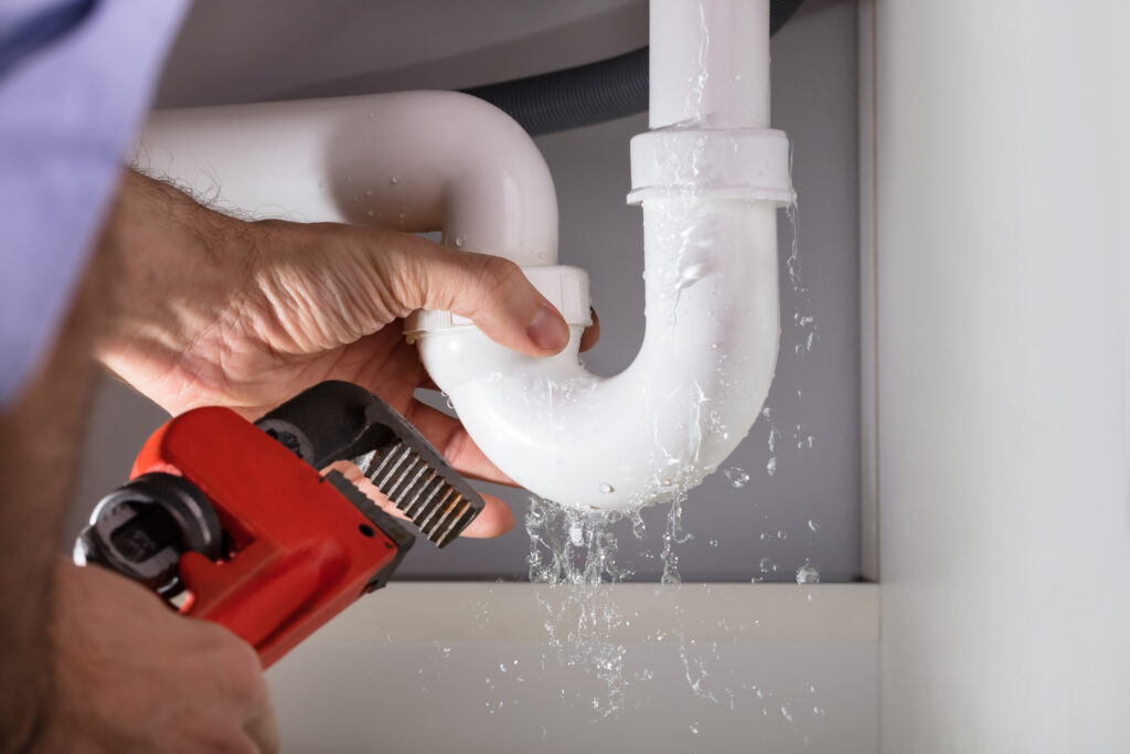 Close-up of plumber's hands fixing white sink pipe with red adjustable wrench.