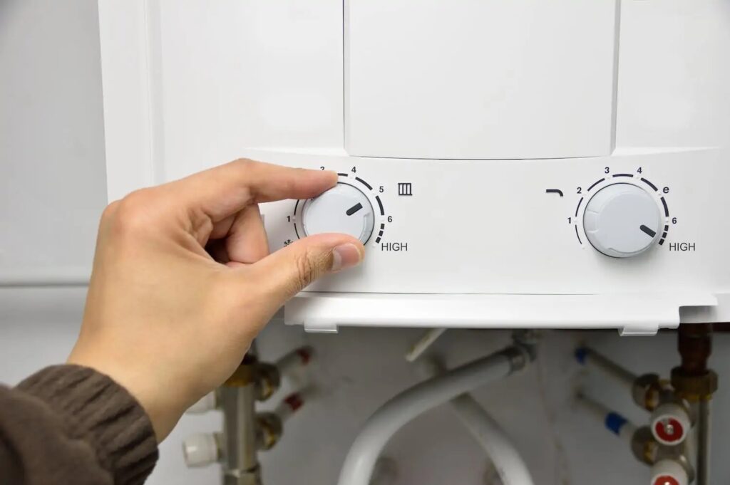 Hand turning a knob on a white tankless water heater.
